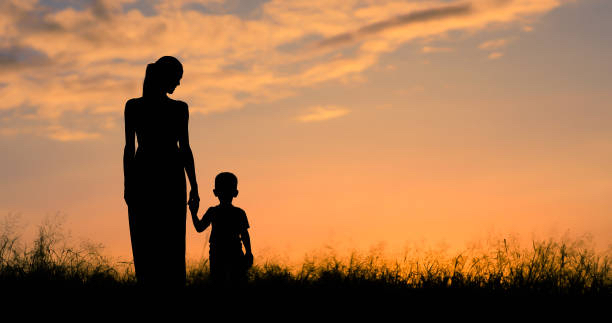 Mother and child silhouette walking in a field at sunset.